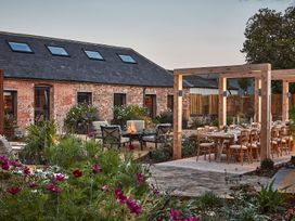 An outdoor seating area with chairs around a fire pit and a dining table under wooden pergolas at The Stables at Galteemore Farm in Avebury near Marlborough