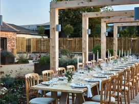 An outdoor dining area with a long wooden table set with plates glasses and candles surrounded by wooden chairs at The Stables in Galteemore Farm in Avebury near Marlborough