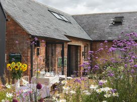 An outdoor patio with flowers and tables in front of a brick building with skylights at The Stables Galteemore Farm in Avebury near Marlborough