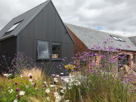 A garden with purple and white flowers in front of a dark gray building and a brick building at The Stables in Galteemore Farm in Avebury near Marlborough