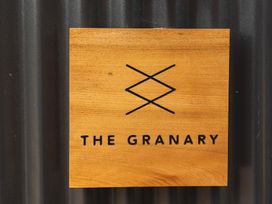 A wooden sign with a black geometric logo and the text the granary