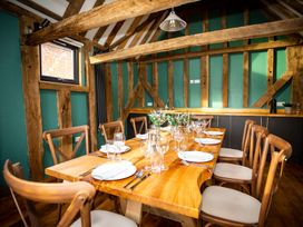A dining room with a wooden table set for eight with plates glasses and flowers at The Stables in Galteemore Farm in Avebury near Marlborough