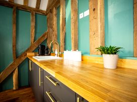 A kitchen countertop with a sink coffee makers canisters and a plant against green walls with wooden beams at The Stables Galteemore Farm in Avebury near Marlborough