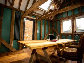 A wooden table with a laptop cup and pitcher in a room with exposed wooden beams and green walls at The Stables Galteemore Farm in Avebury near Marlborough