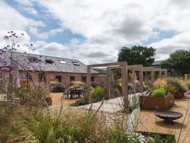 An outdoor garden area with wooden pergolas tables and chairs surrounded by plants and flowers at The Stables Galteemore Farm in Avebury near Marlborough