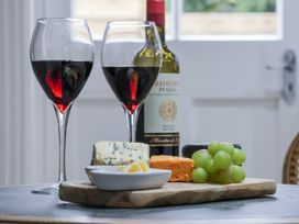 Two glasses of red wine with a bottle of wine cheese and grapes on a wooden board at Fern Cottage in North Dalton near Great Driffield