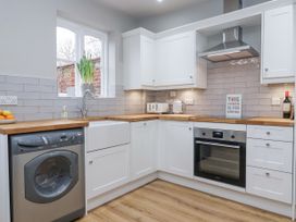 A kitchen with white cabinets wooden countertops a washing machine an oven a sink a range hood and a window at Fern Cottage in North Dalton near Great Driffield