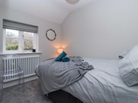 A bedroom with a bed covered with gray and white bedding a window with a gray blind a transparent chair a radiator a wall mirror and a lamp at Fern Cottage in North Dalton near Great Driffield