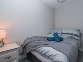 A bedroom with a bed covered in gray bedding and two rolled blue towels on top next to a white nightstand with a lamp at Fern Cottage in North Dalton near Great Driffield