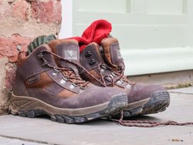A pair of brown hiking boots with red and green socks inside placed on a floor near a brick wall and a light green door at Fern Cottage in North Dalton near Great Driffield