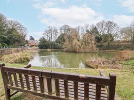 A wooden bench facing a pond surrounded by trees and grass near a brick building at Fern Cottage in North Dalton near Great Driffield