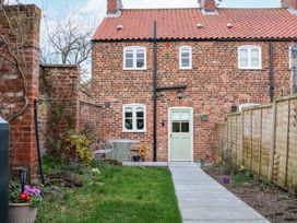 A backyard with a grass lawn path leading to a brick house with white windows and a green door at Fern Cottage in North Dalton near Great Driffield