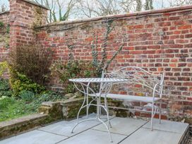 A metal table and bench set on a patio next to a brick wall with plants growing at Fern Cottage in North Dalton near Great Driffield
