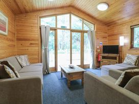 A living room with sofas coffee table television and large windows at Rowan Lodge in Rosliston
