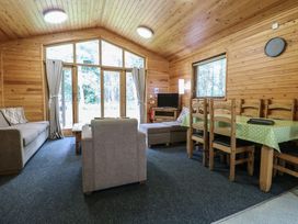 A living room with sofas a dining table and chairs with a green tablecloth and large windows at Rowan Lodge in Rosliston