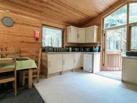 A kitchen with light wooden cabinets a dining table with chairs and a door leading outside at Rowan Lodge in Rosliston