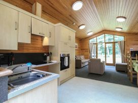 A kitchen and living area with a sink oven sofa armchair dining table and large windows at Rowan Lodge in Rosliston