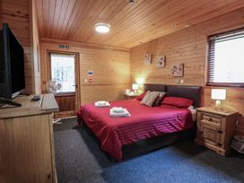 A bedroom with a double bed red bedding wooden furniture and a door at Rowan Lodge in Rosliston