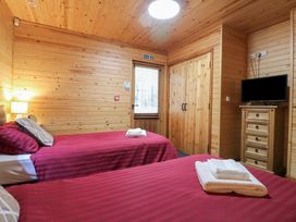 A bedroom with two single beds with red striped bedding a wooden wardrobe a TV on a wooden chest of drawers and wooden walls and ceiling at Rowan Lodge in Rosliston