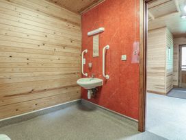 A small washbasin with handrails and a mirror on a red wall in a wooden room at Rowan Lodge in Rosliston