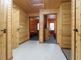 A corridor with wooden walls and ceiling leading to bedrooms with red bedding at Rowan Lodge in Rosliston