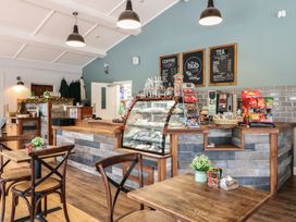 A cafe counter with display case snacks tables and chairs with menus on the wall at Rowan Lodge in Rosliston