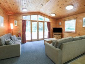 A wooden living room with two gray sofas a wooden coffee table a TV on a wooden stand and large glass doors at Oak Lodge in Rosliston