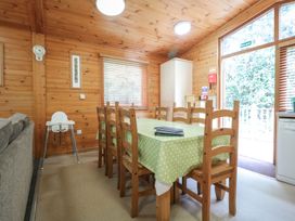 A dining area with wooden chairs around a table with a green polka dot tablecloth and a high chair by the window at Oak Lodge in Rosliston
