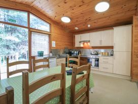 A kitchen with wooden chairs around a table covered with a green polka dot tablecloth at Oak Lodge in Rosliston