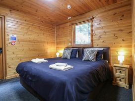 A bedroom with wooden walls a large bed blue bedding pillows bedside tables and lamps at Oak Lodge in Rosliston