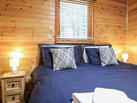 A bedroom with a double bed blue bedding two pillows bedside tables with lamps and wood paneled walls at Oak Lodge in Rosliston