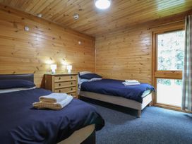 A bedroom with two single beds with dark bedding a wooden chest of drawers with two lamps and a window at Oak Lodge in Rosliston