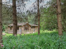 A wooden cabin surrounded by trees and plants with a wooden deck at Oak Lodge in Rosliston