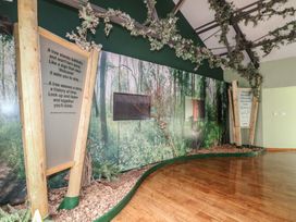 An indoor space with a forest-themed wall mural two large wooden framed signs and artificial ivy on ceiling beams at Oak Lodge in Rosliston