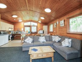 A wooden lodge interior with a gray sectional sofa white patterned cushions wooden coffee table kitchen area and dining table with chairs at Chestnut Lodge in Rosliston
