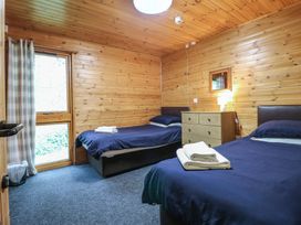 A bedroom with two single beds with blue bedding a wooden chest of drawers and a window with checked curtains at Chestnut Lodge in Rosliston