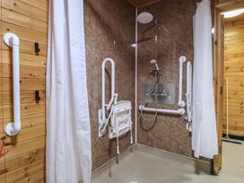 A bathroom shower area with wall-mounted foldable seat and grab bars at Chestnut Lodge in Rosliston
