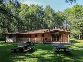 A wooden lodge with a porch and picnic tables on a grassy area surrounded by trees at Chestnut Lodge in Rosliston