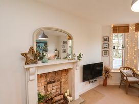 A living room with a brick fireplace a wall-mounted TV and a wooden chair by windows at Happy Days in Scarborough