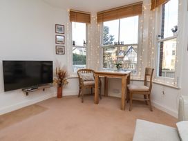 A corner of a room with a wooden table and two chairs near windows with blinds and string lights a wall-mounted TV and framed pictures on the wall at Happy Days in Scarborough