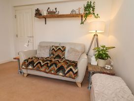 A living room with a sofa covered with patterned throw and pillows a wooden shelf with decorative items a lamp and plants at Happy Days in Scarborough