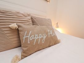 A bed with a beige pillow with tassels and the words Happy Place with two beige ribbed pillows behind at Happy Days in Scarborough