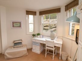 A study area with a white desk and chair by windows with wooden blinds and a small cushioned seat with a pillow at Happy Days in Scarborough