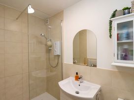 A bathroom with a shower area with a glass screen a white sink with a mirror above it and a wall cabinet with plants on top at Happy Days in Scarborough
