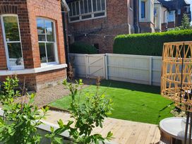A small garden with artificial grass a white wooden fence and gate a brick house with windows and green plants at Happy Days in Scarborough