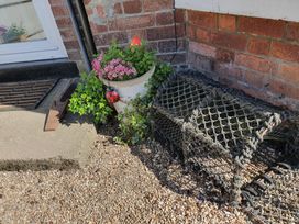 An outdoor corner with a flower pot containing pink flowers and greenery a lobster pot on gravel and a door mat at Happy Days in Scarborough