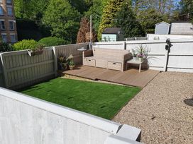 A small outdoor patio with a wicker sofa table plants artificial grass and gravel at Happy Days in Scarborough