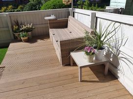 An outdoor wooden deck with a wicker sofa a small side table with potted plants and a white fence surrounding the area at Happy Days in Scarborough