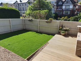 A fenced backyard with artificial grass, a wooden deck, potted plants, and surrounding residential buildings at Happy Days in Scarborough