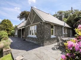 An exterior view of a stone house with a slate roof and a patio with outdoor table and chairs surrounded by plants and trees at Bryn Awelon in Harlech